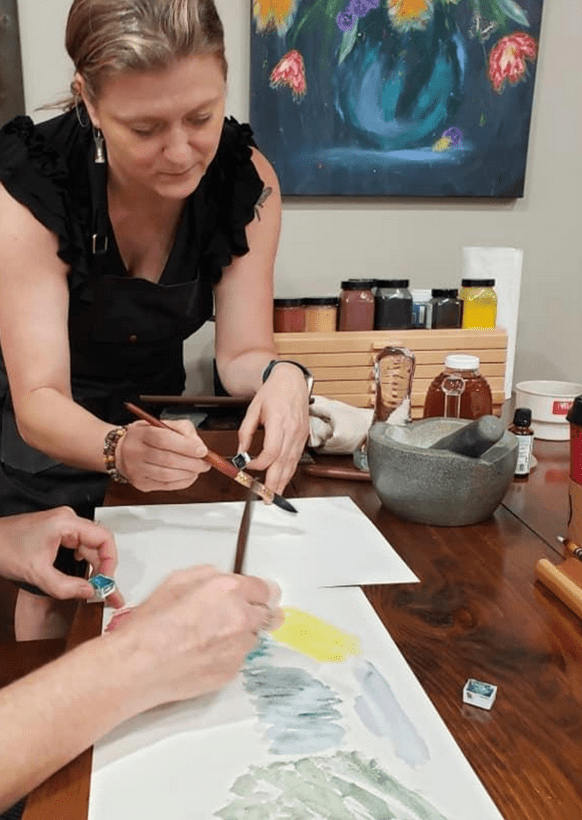 Two women engaged in painting together at a table, showcasing creativity and teamwork in their artistic process.