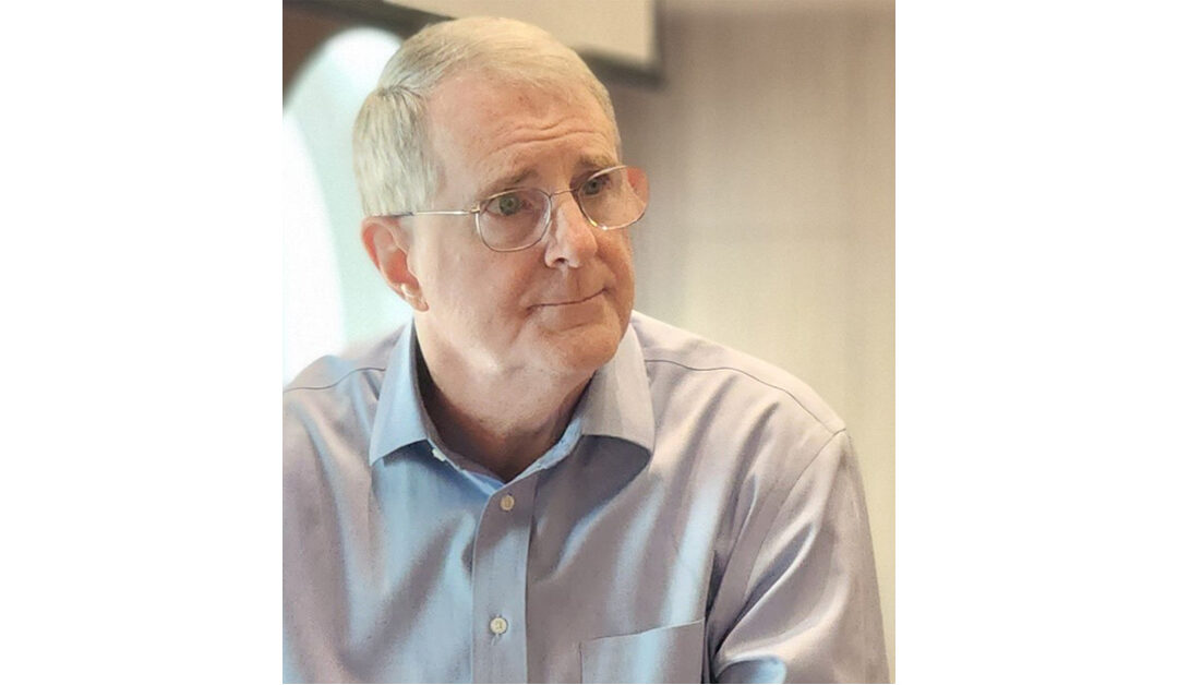 Board Member John Gaffney, wearing glasses and a blue shirt, is captured looking off to the side with a thoughtful expression.